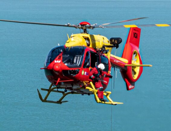 Rescue helicopter flying towards the camera with a crew person standing on the skids