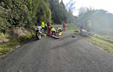 A crash scene. Paramedics and fire brigade treating a man on the road with a crashed bike beside them.