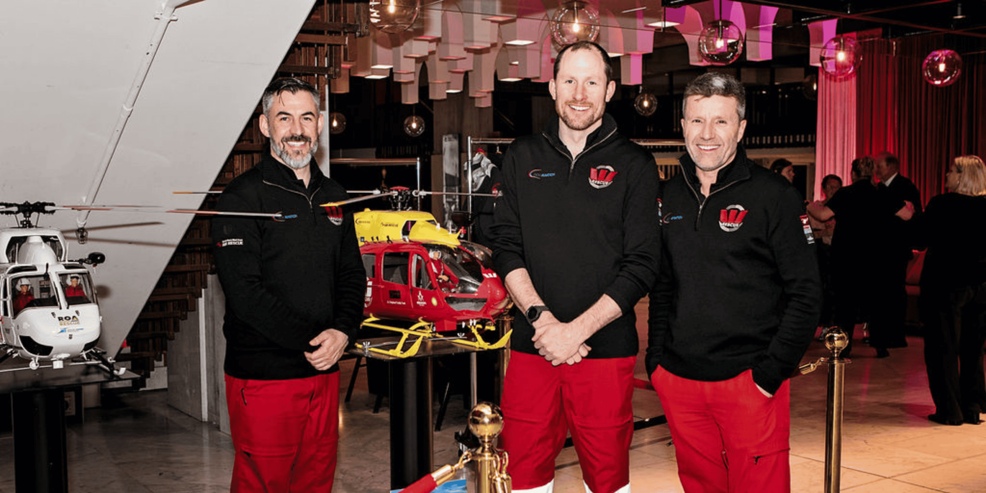 3 rescue pilots in front of model helicopters