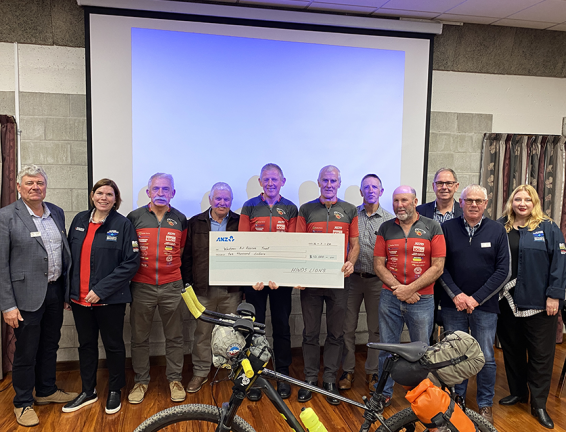 A group of cyclists with a large cheque