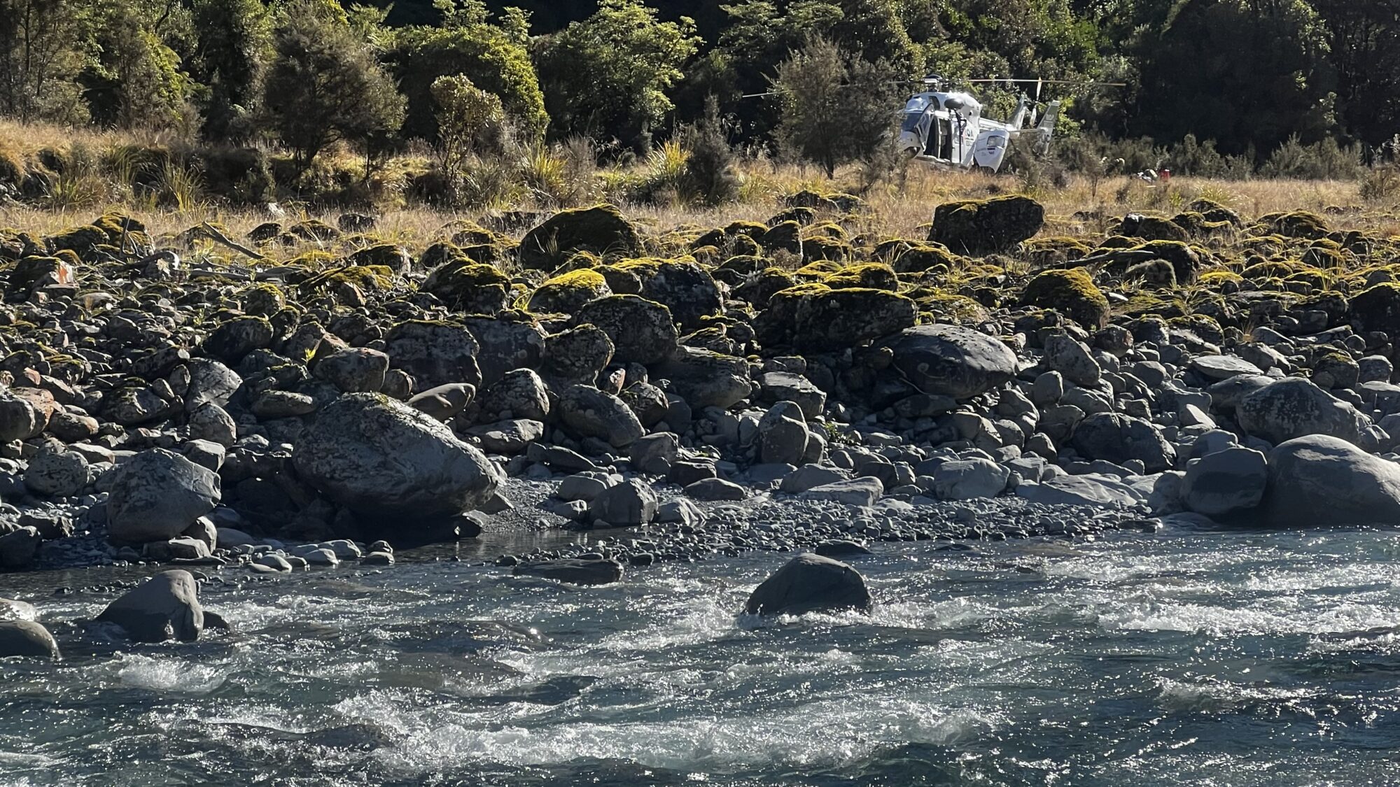 White rescue helicopter sitting on the ground on the other side of a river