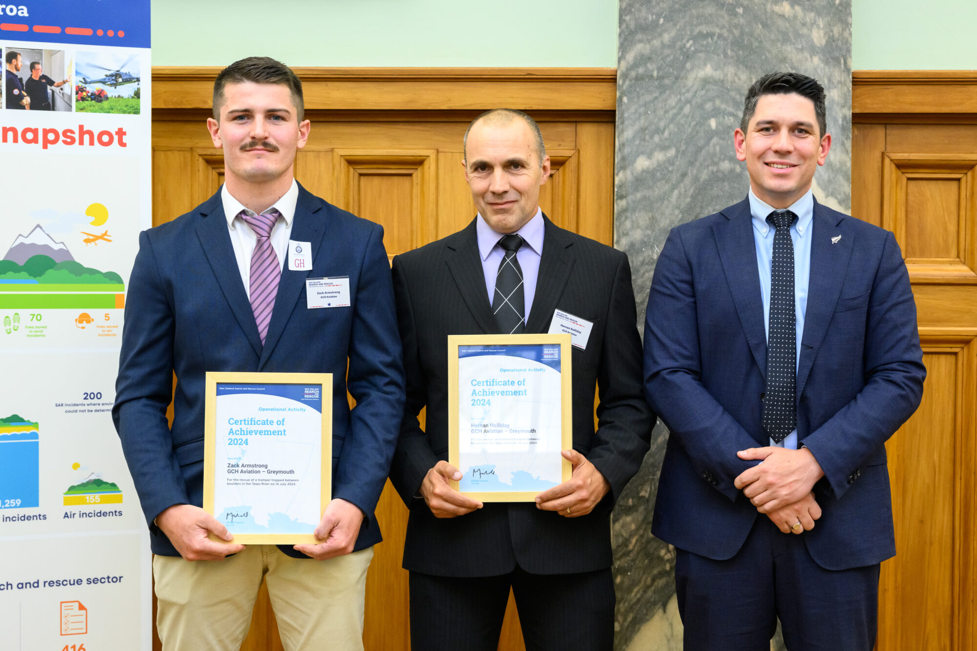 three men in suits, two holding framed awards